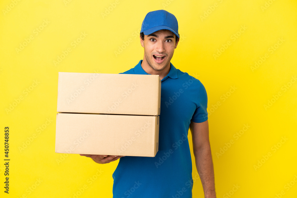 Delivery man over isolated yellow wall with surprise facial expression