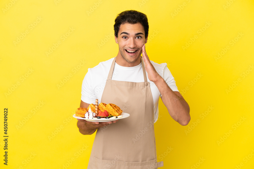 Restaurant waiter holding waffles over isolated yellow background with surprise and shocked facial expression Restaurant waiter holding waffles over isolated yellow background with surprise and shocked facial expression