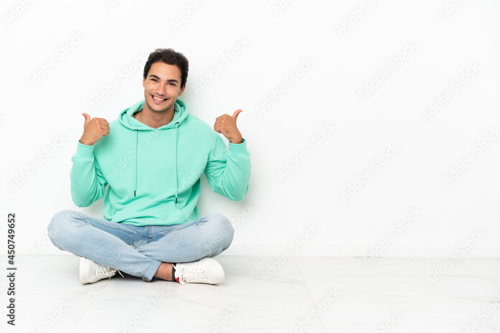 Caucasian handsome man sitting on the floor with thumbs up gesture and smiling Caucasian handsome man sitting on the floor with thumbs up gesture and smiling