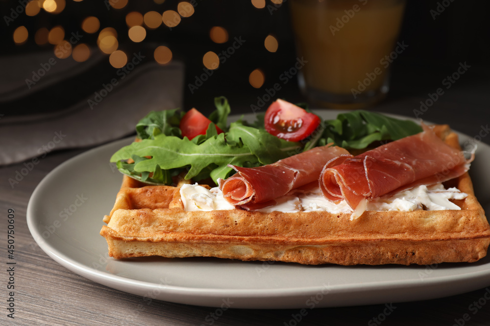 Delicious waffle with cheese, prosciutto, tomatoes and arugula on wooden table