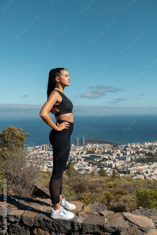  photograph of a girl in black sportswear practicing yoga and sports outdoors with beautiful views behind her