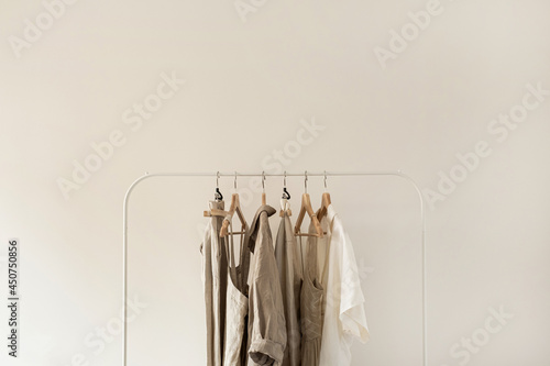 Minimal aesthetic fashion clothes concept. Neutral beige washed linen female blouses, dresses and t-shirts on hanger on white background. Fashion blog, website, social media photo