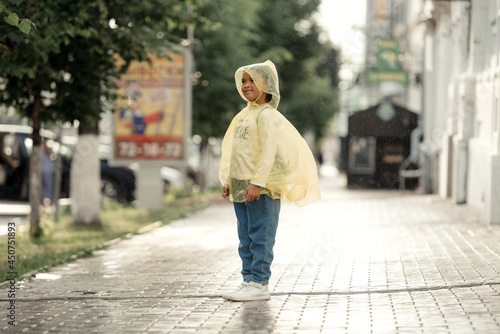 Happy funny child under the autumn shower. Girl is wearing yellow raincoat and enjoying rainfall.