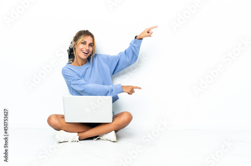 Young blonde Uruguayan girl with the laptop isolated on white background pointing finger to the side and presenting a product © luismolinero