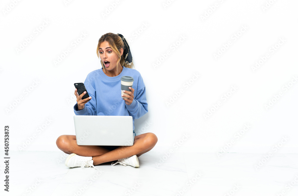 Young blonde Uruguayan girl with the laptop isolated on white background holding coffee to take away and a mobile