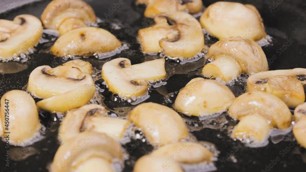 Sliced champignon mushrooms are fried in a hot pan in close up. Golden slices of champignons are fried in olive oil. Beautiful wallpaper of cooking for restaurant. Slow motion. Sliced champignon mushrooms are fried in a hot pan in close up. Golden slices of champignons are fried in olive oil. Beautiful wallpaper of cooking for restaurant. Slow motion.
