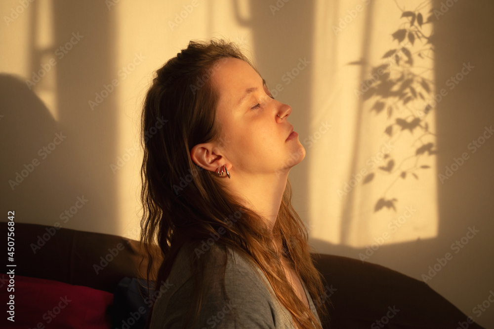 Young woman close eyes and relaxation in warm rays of sunset. Warm calm portrait of girl indoor Young woman close eyes and relaxation in warm rays of sunset. Warm calm portrait of girl indoor