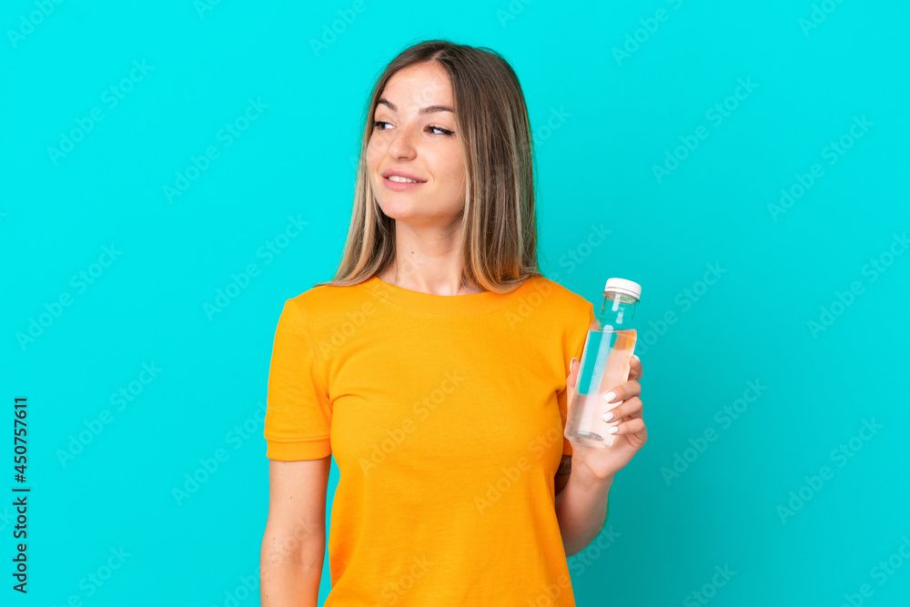 Young Romanian woman with a bottle of water isolated on blue background looking to the side and smiling Young Romanian woman with a bottle of water isolated on blue background looking to the side and smiling