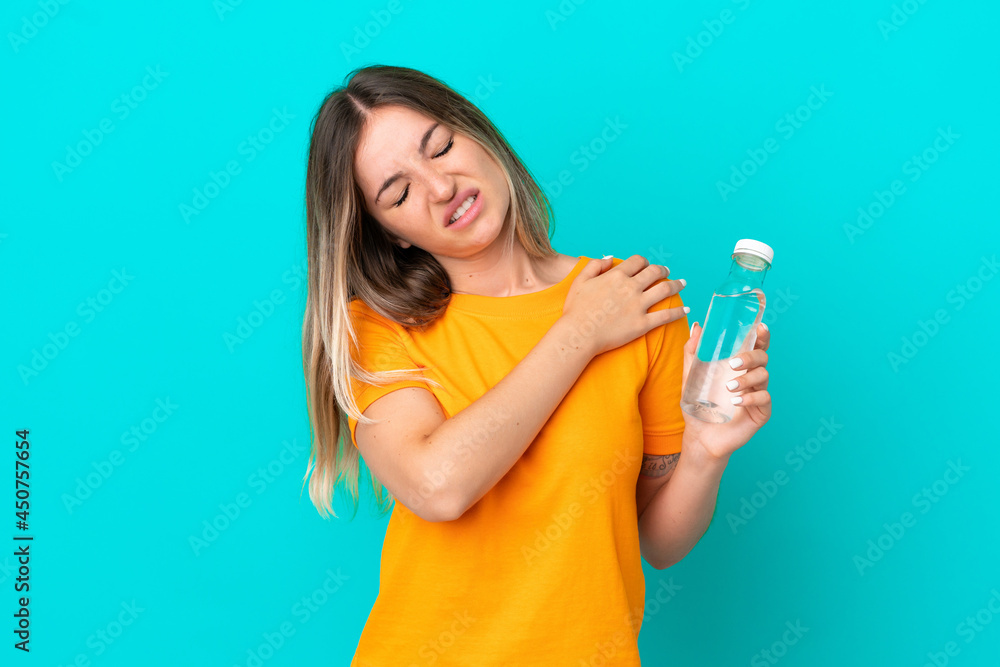 Young Romanian woman with a bottle of water isolated on blue background suffering from pain in shoulder for having made an effort Young Romanian woman with a bottle of water isolated on blue background suffering from pain in shoulder for having made an effort