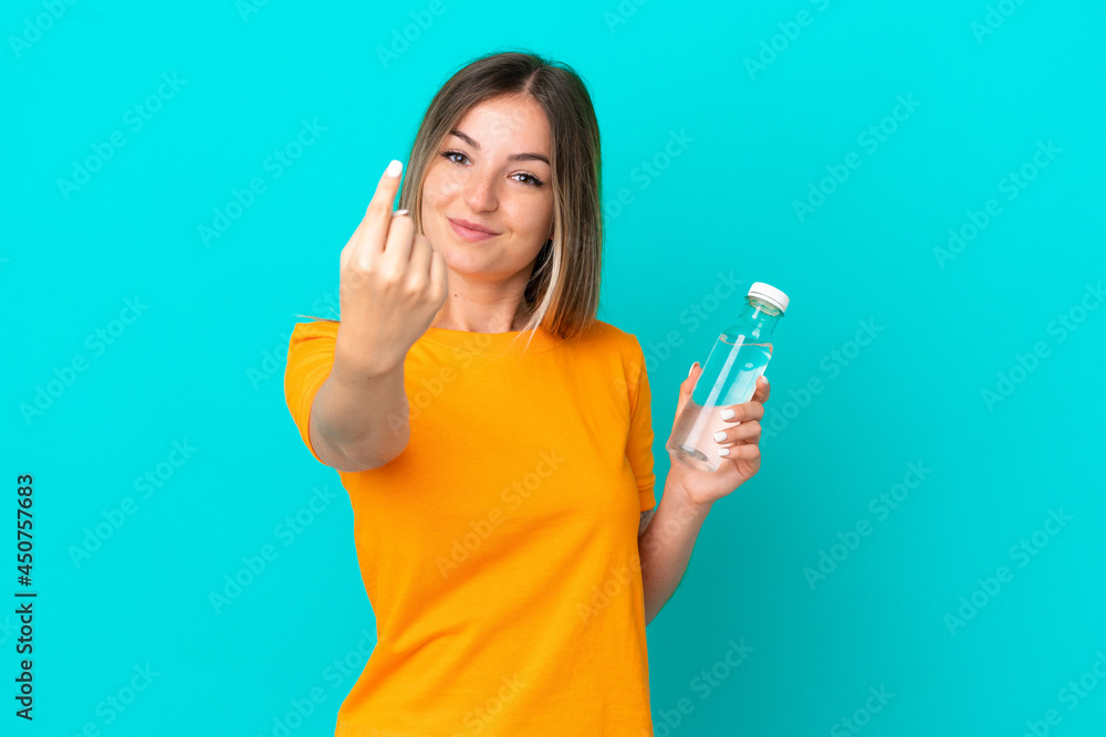 Young Romanian woman with a bottle of water isolated on blue background doing coming gesture Young Romanian woman with a bottle of water isolated on blue background doing coming gesture