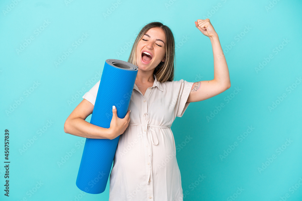 Young Romanian woman isolated on blue background pregnant and doing strong gesture while going to yoga classes Young Romanian woman isolated on blue background pregnant and doing strong gesture while going to yoga classes