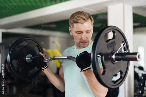 Athlete man lifting barbells working out with curl bar in the gym doing elevations. Caucasian male training in the gym during the day