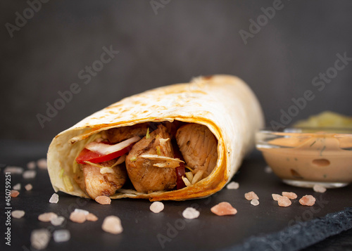 Shawarma with chicken and vegetables in pita bread on a slate board. Himmalay salt scattered around, special sauces in sauce bowls photo