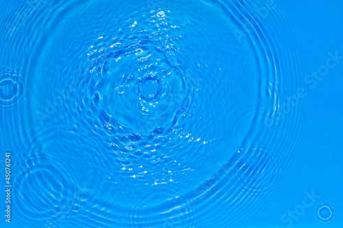Surface of bright blue transparent swimming pool water texture with circles on the water. Trendy abstract nature background. Water waves in sun light reflections