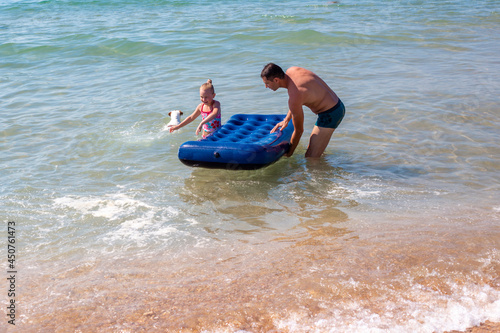 Dad and daughter in the sea ride on a rubber mattress. Summer fun holidays.