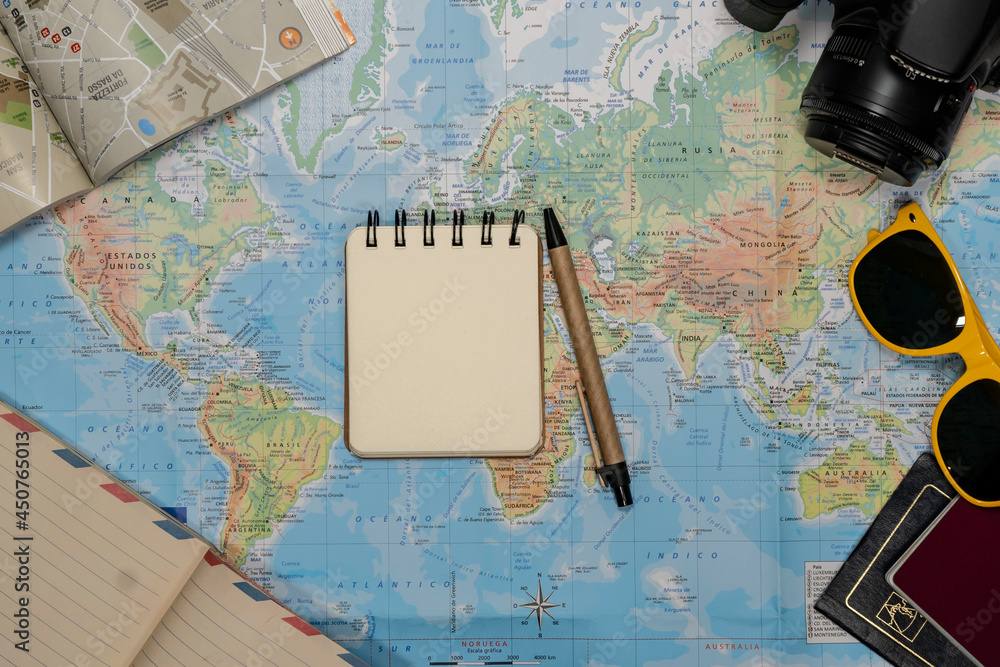 Fototapeta Travel Flat lay of an empty notebook, sunglasses, passport, camera over a world map