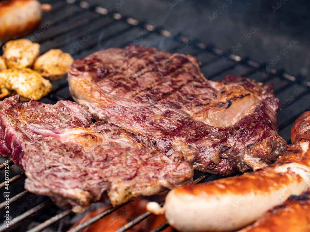 Barbecue in the summer. Close-up of grilled steaks. The meat is rare inside and roasted on the outside. Some sausages in the foreground.