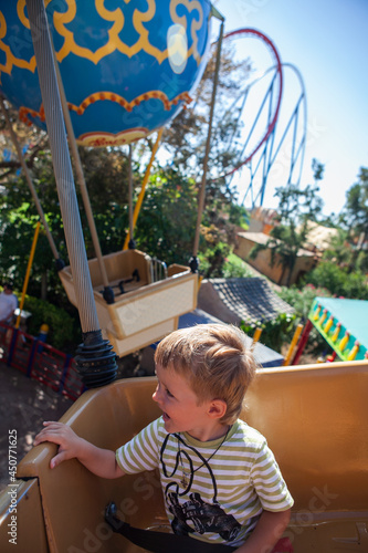 Vertical photo boy toddler sits at a booth in the carrousel. Happy baby is at at amusement park . Smiling boy rides art attraction in a fairground. Leisure with family. photo