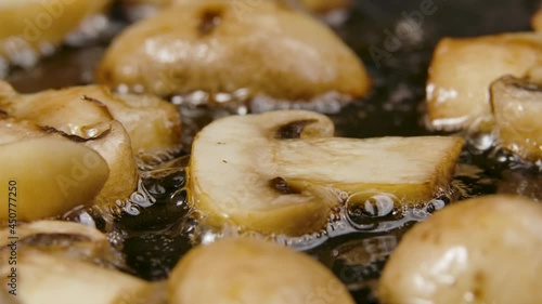 Golden slices of champignons are fried into a hot pan with oilin close up. Sprinkle the cooked mushrooms with seasoning. Preparing vegetables for cooking dinner. Slow motion. photo