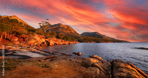 Landscape view of natural sea coast with mountain range in evening sunset  in orange-red and blue colors. Freycinet National Park Hazard mountain range, Freycinet National Park, Tasmania, Australia.