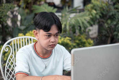 A young man attends an online class via his laptop while hanging out at his yard or resort. Modern remote education concept. photo