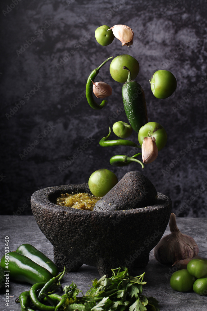 Salsa verde mexicana en molcajete con ingredientes cayendo. Chiles