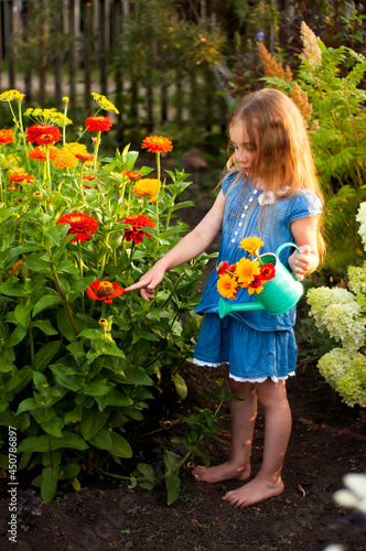 Little girl in a blue dress examines flowers in the garden