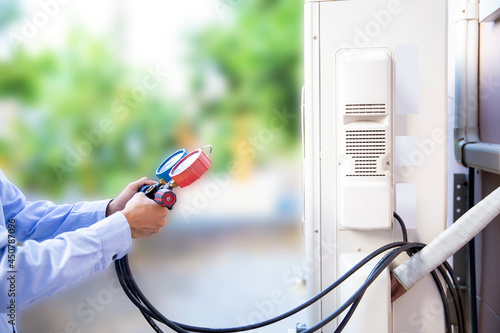 Mechanic air repair using manifold gauge for filling home air conditioner and checking maintenance outdoor air compressor unit.