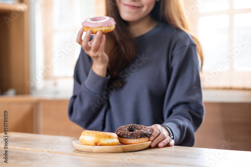 Closeup image of a beautiful young asian woman holding and enjoyed eating donuts at home