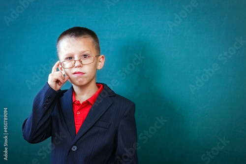 A Happy child child standing at the blackboard with a school backpack wearing glasses