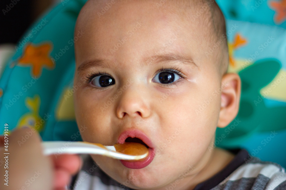 Little baby is spoon fed. Mother feeding her child with baby food - pureed vegetables and fruits Little baby is spoon fed. Mother feeding her child with baby food - pureed vegetables and fruits