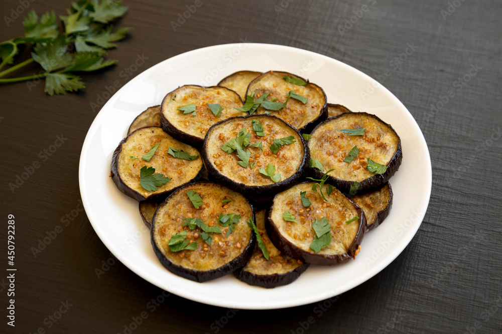 Homemade Organic Roasted Eggplant on a white plate on a black background, side view. Homemade Organic Roasted Eggplant on a white plate on a black background, side view.