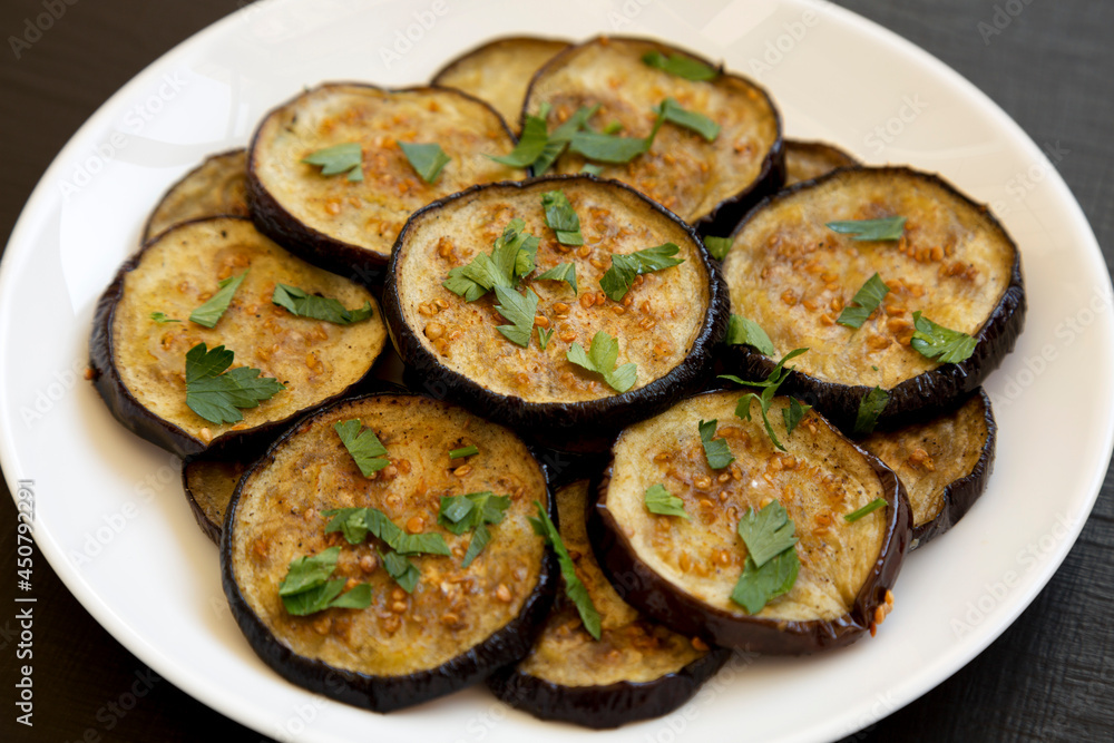 Homemade Organic Roasted Eggplant on a white plate on a black background, side view. Close-up. Homemade Organic Roasted Eggplant on a white plate on a black background, side view. Close-up.