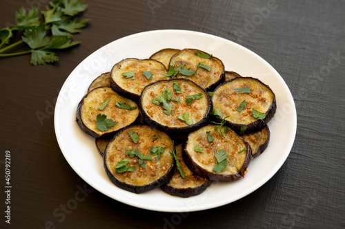 Homemade Organic Roasted Eggplant on a white plate on a black background, side view.