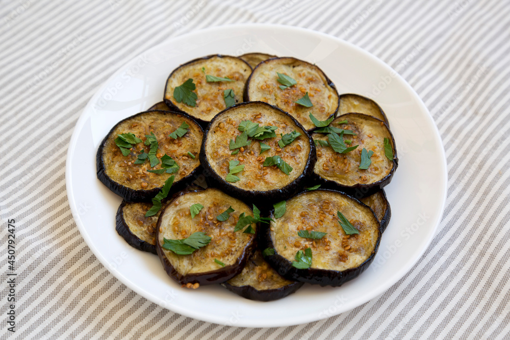 Homemade Organic Roasted Eggplant on a white plate on a white wooden background, side view.