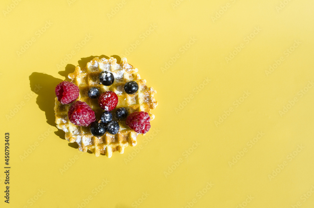 A waffle with different berries of black and red color on a yellow background is hard light. Homemade cakes crispy waffle on a colored background copy space