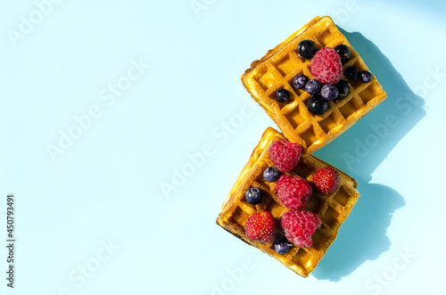 Fresh waffles with different berries of black and red color on a blue background hard light. Homemade cakes crispy waffles on a colored background copy space