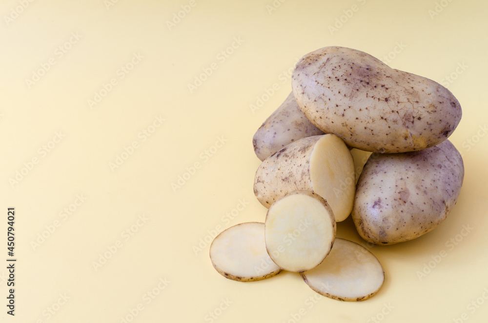 Fototapeta premium Potato tubers and half a potato on a colored background. Potatoes on a colored background of kopi space 