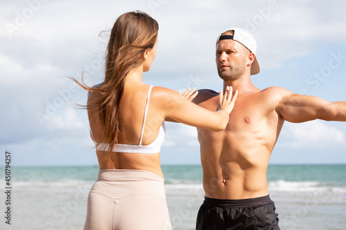 young man stretching and exercising outdoors from trainer suggesting on the beach