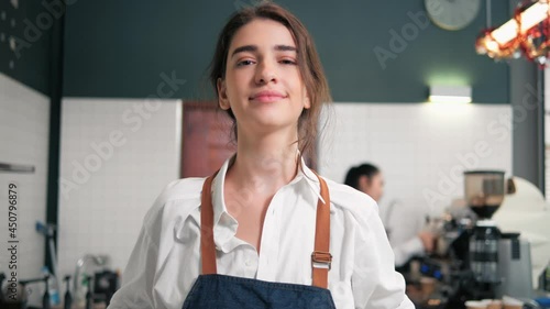 Portrait of young barista wearing apron and looking at camera. Excited small business owner.