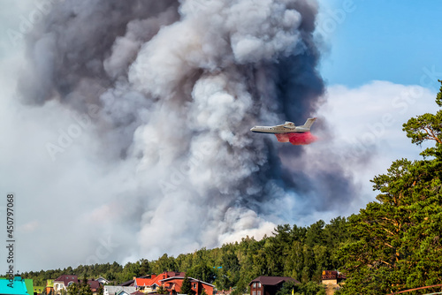 Big amphibious fire aircraft drops water on large forest fire near the village
