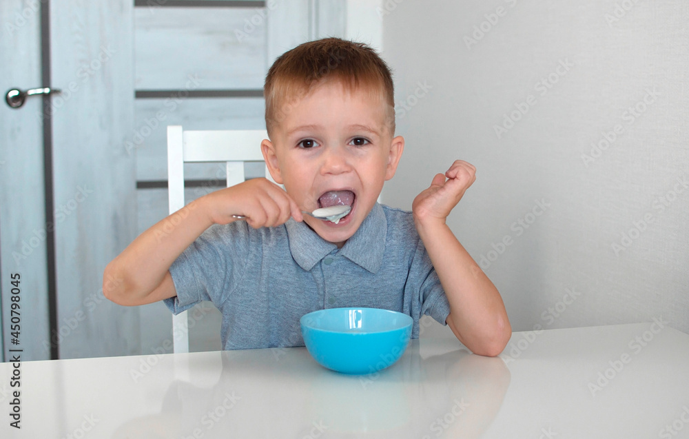 A happy child eats a healthy delicious breakfast. Portrait of a child having breakfast. A cute happy baby is sitting in the kitchen and learning with a spoon. Selective focus. A happy child eats a healthy delicious breakfast. Portrait of a child having breakfast. A cute happy baby is sitting in the kitchen and learning with a spoon. Selective focus.