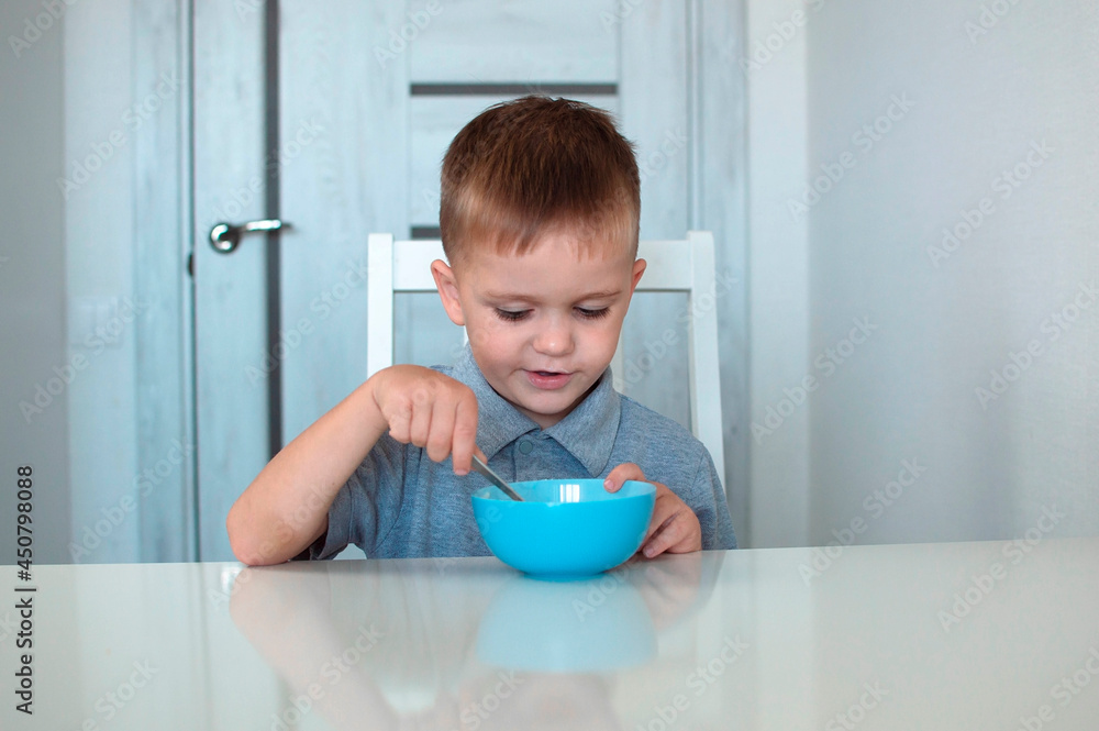 A happy child eats a healthy delicious breakfast. Portrait of a child having breakfast. A cute happy baby is sitting in the kitchen and learning with a spoon. Selective focus. A happy child eats a healthy delicious breakfast. Portrait of a child having breakfast. A cute happy baby is sitting in the kitchen and learning with a spoon. Selective focus.