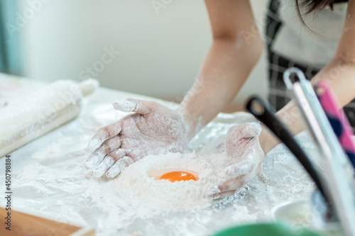 A woman is mixing flour and eggs with her hands before kneading the dough to make bread.