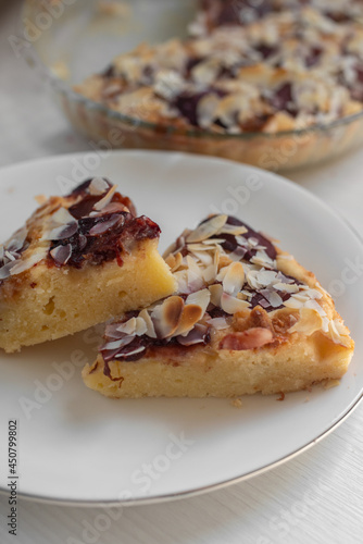 Sliced plum-marzipan pie on a white wooden table. Almond on top.