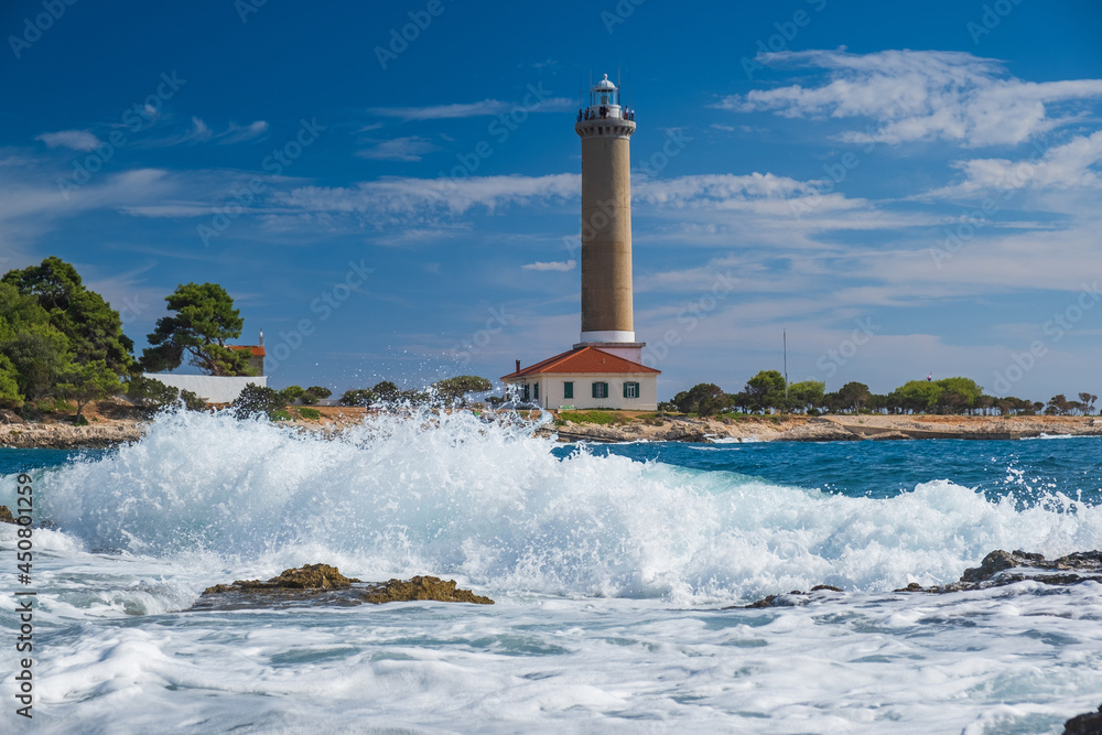 Sea waves breaking on rocks, lighthouse of Veli Rat on the island of Dugi Otok, Croatia in background