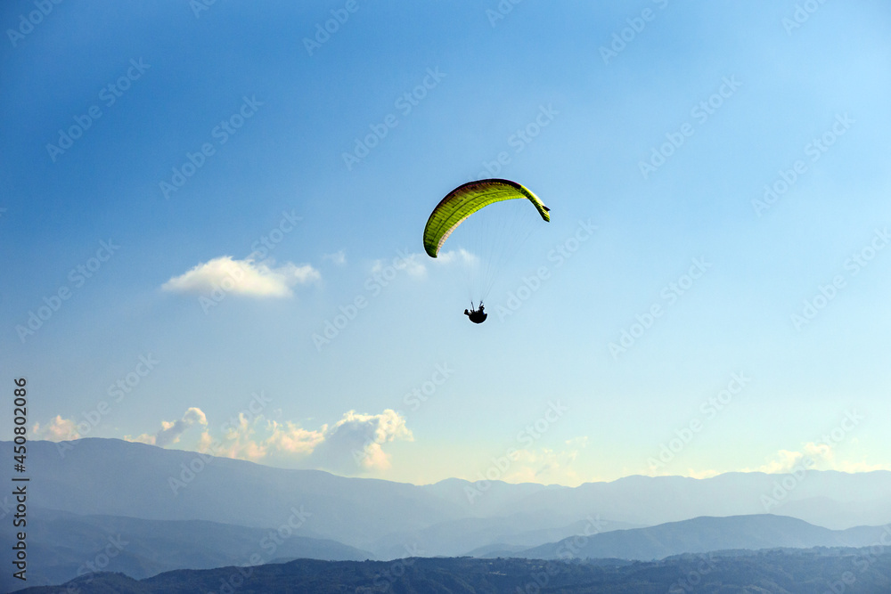 A yellow paraglider is flying over the mountain