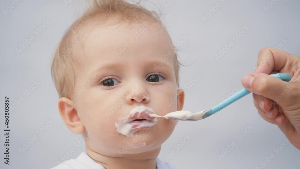 mother feeds her little son from a spoon with porridge. The kid is eating breakfast from a spoon. loving mother takes care of the child, spoon feeds porridge. Handsome smiling cute kid. Children food mother feeds her little son from a spoon with porridge. The kid is eating breakfast from a spoon. loving mother takes care of the child, spoon feeds porridge. Handsome smiling cute kid. Children food