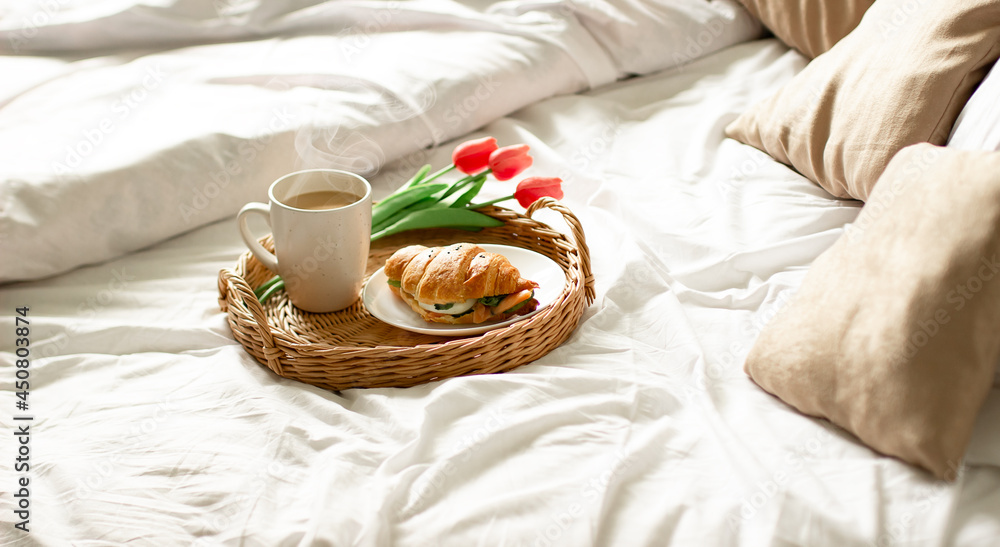 Breakfast tray on the bed in the hotel room. breakfast in a snow-white bed, coffee with a croissant on a wicker tray. Morning Breakfast tray on the bed in the hotel room. breakfast in a snow-white bed, coffee with a croissant on a wicker tray. Morning