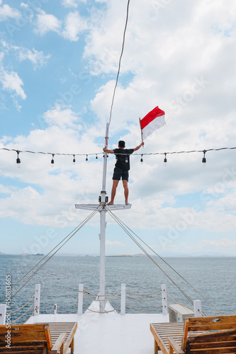 A man standing on pole ship and waving indonesian flag
